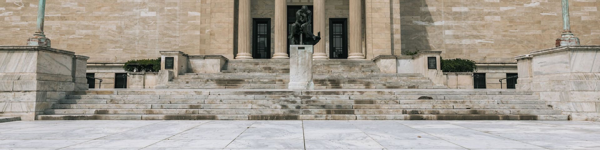 A neoclassical building with a central entrance flanked by columns, a statue, and steps leading up to it.