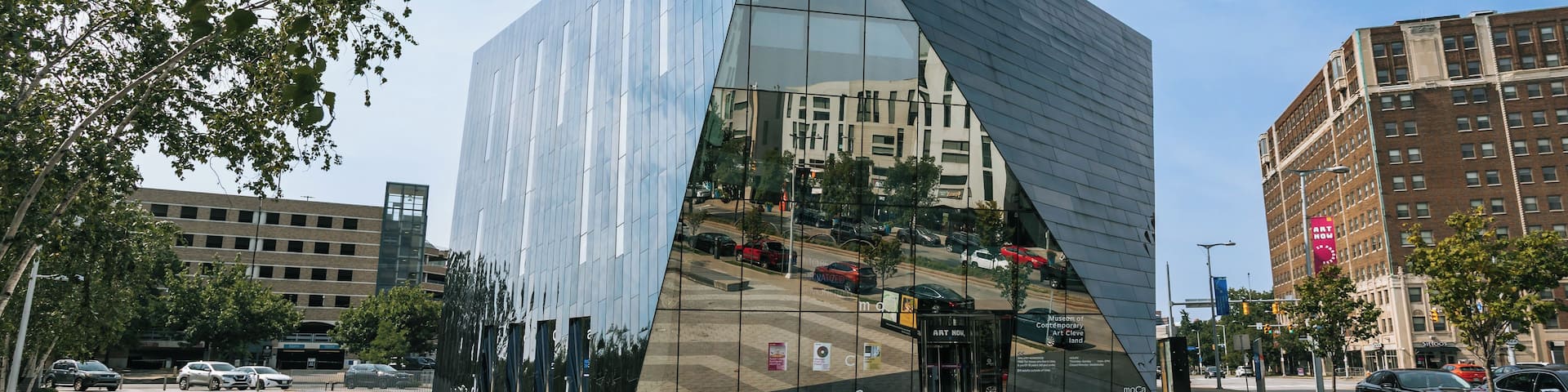 A modern glass building with a triangular facade, surrounded by urban streets and other buildings.