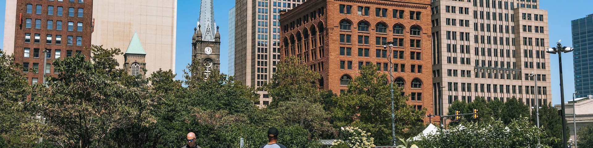 Un paysage urbain avec des gratte-ciel modernes, une tour de l’horloge historique et une promenade pavée où l’on peut voir des piétons.
