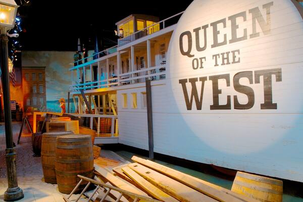 Une maquette du navire « Queen of the West », entourée de barils en bois et d’un lampadaire.