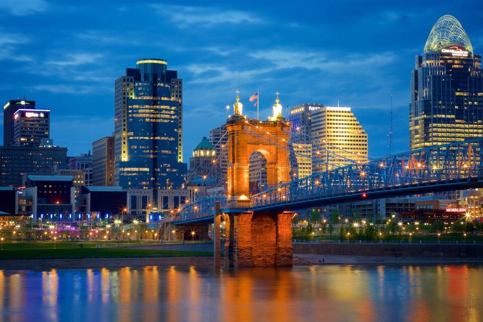 A city skyline with illuminated buildings, a prominent bridge, and a river reflecting the lights.