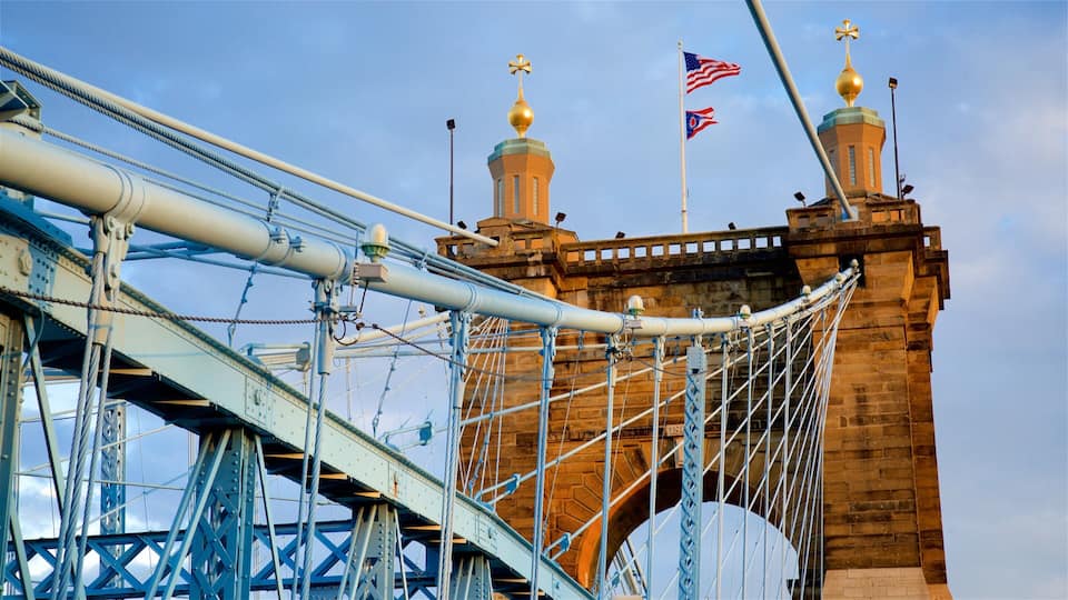 A bridge with blue steel cables and a brick tower with two golden domes and flags.