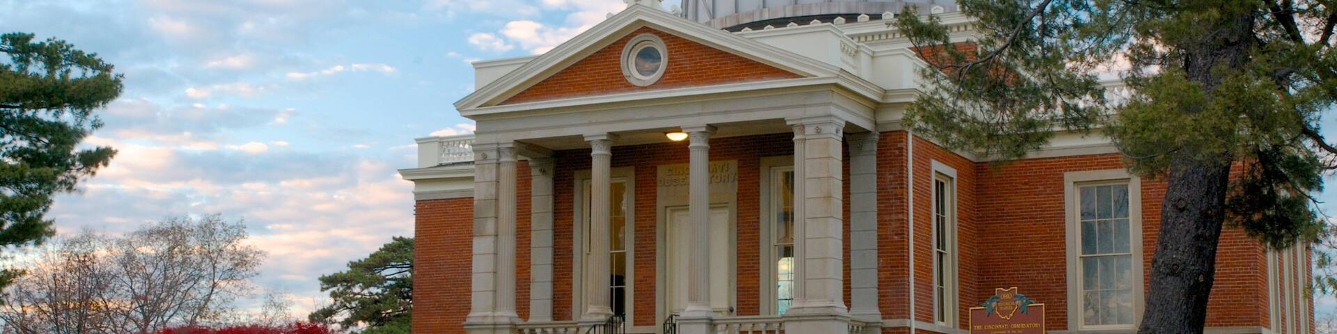 A brick building with a dome and columns, surrounded by trees and a lawn.