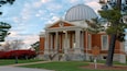 A brick building with a dome and columns, surrounded by trees and a lawn.
