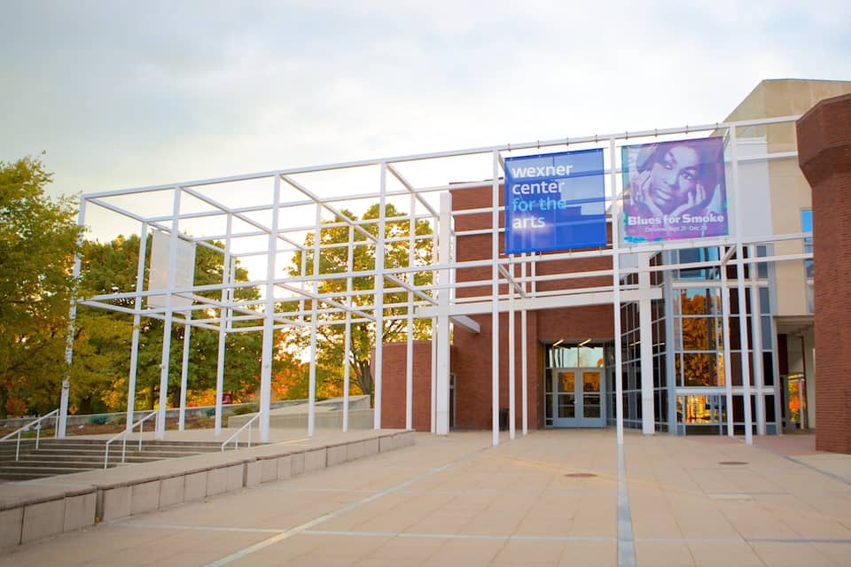 Um edifício moderno com fachada de vidro e uma placa azul que diz “Wexner Center for the Arts”.