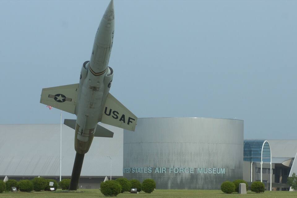 Um grande avião da Força Aérea dos EUA em exposição, com o Museu da Força Aérea dos Estados Unidos ao fundo.