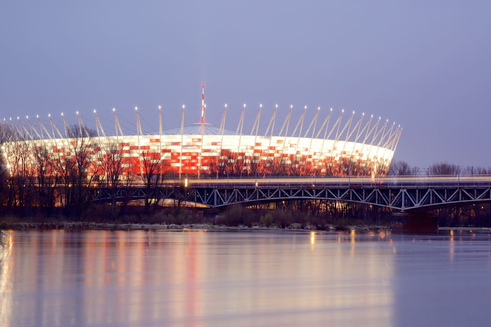A stadium with a distinctive roof structure and a bridge over a body of water.