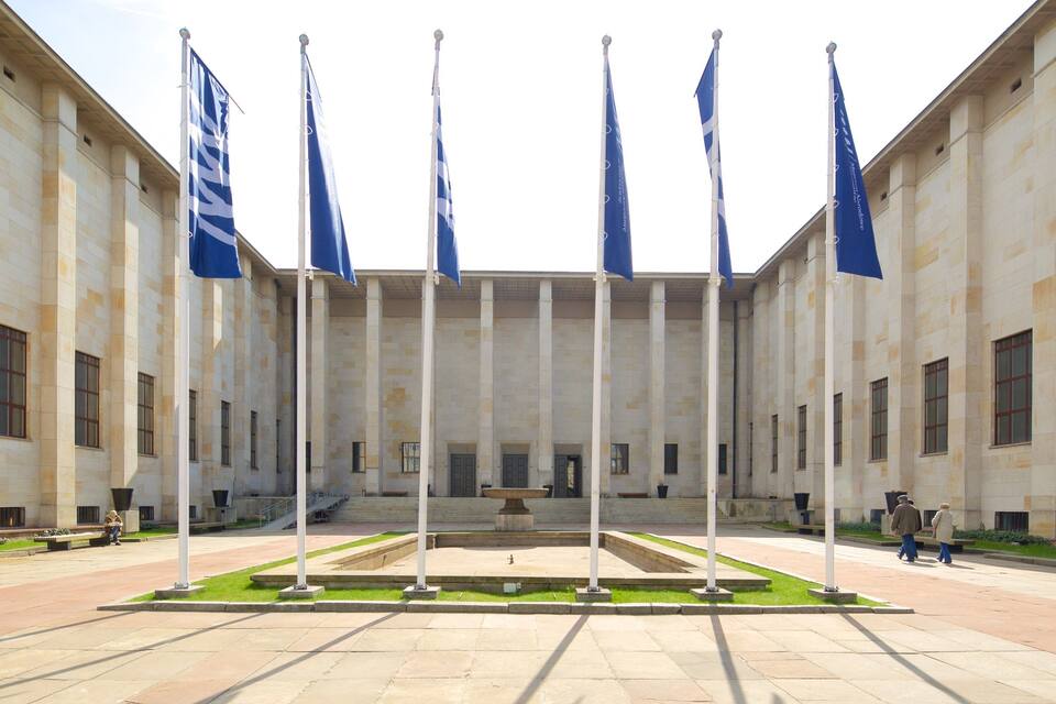 A building with a central courtyard, surrounded by columns, and multiple blue flags.