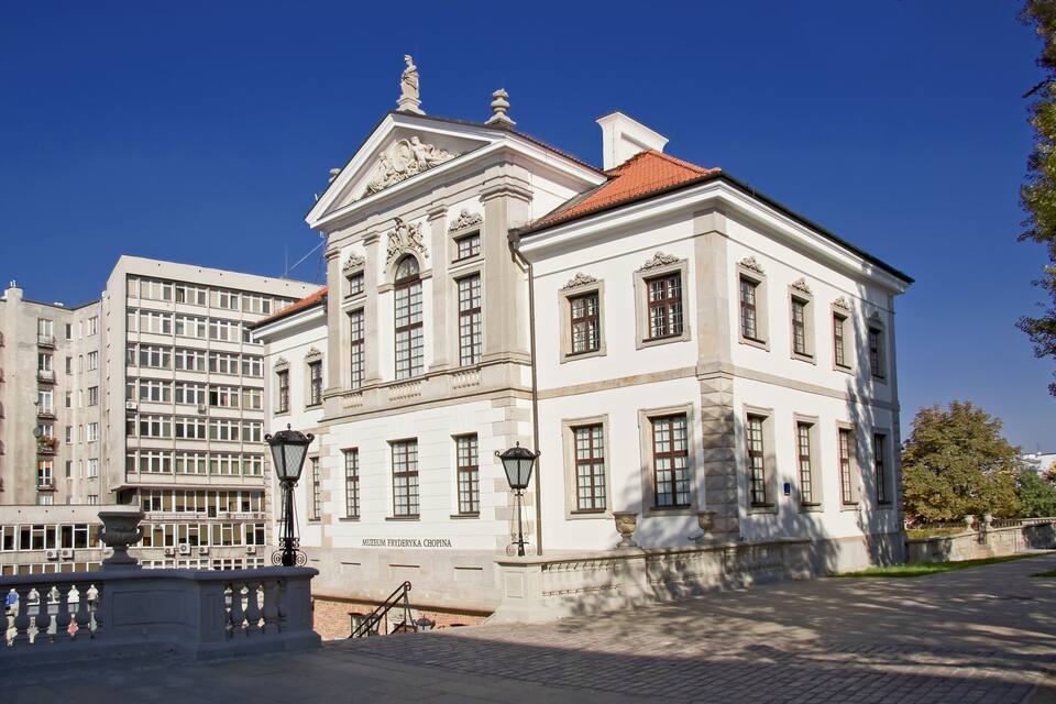 Un edificio histórico con arquitectura clásica, techo de tejas rojas y una placa con el nombre.