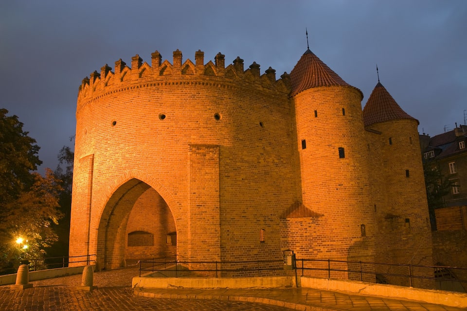 Un castillo de ladrillo histórico con una gran torre central y torres más pequeñas, que presenta merlones y un tejado de tejas rojas.