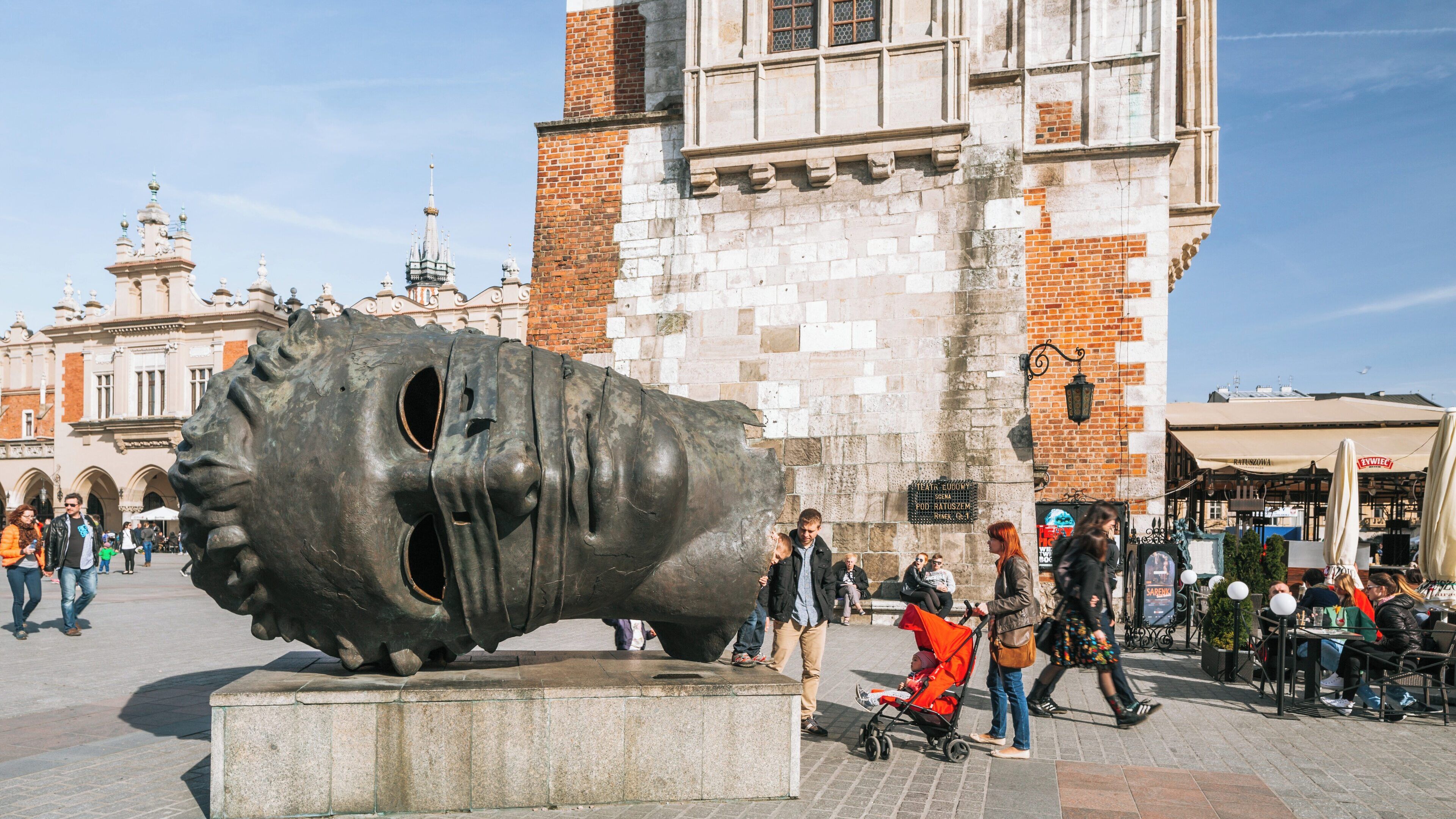 Exploring Main Market Square in Kraków City Centre with modern sculptures and vibrant street life on a sunny day