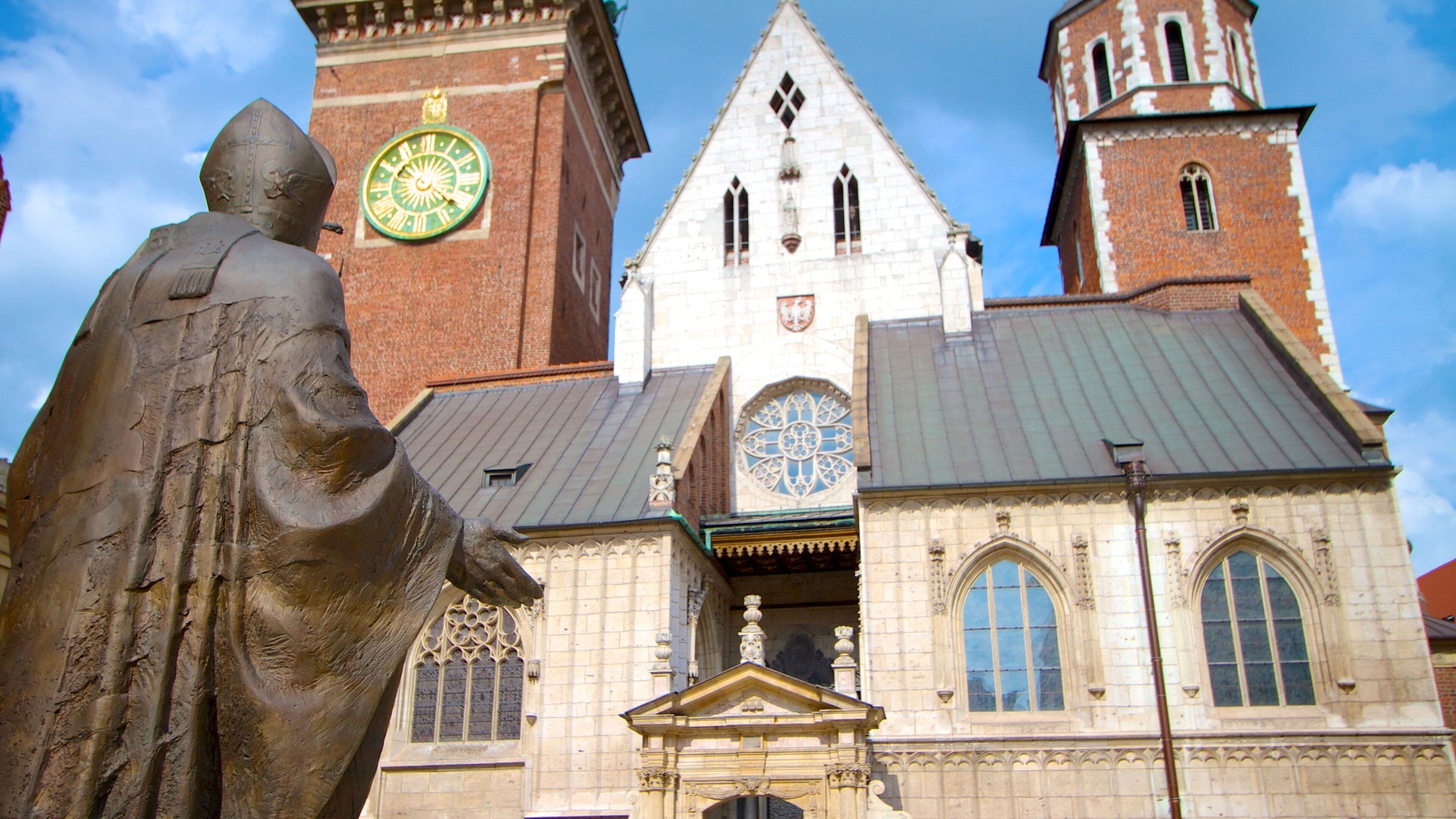 A historical building with a clock tower, a statue, and a rose window.