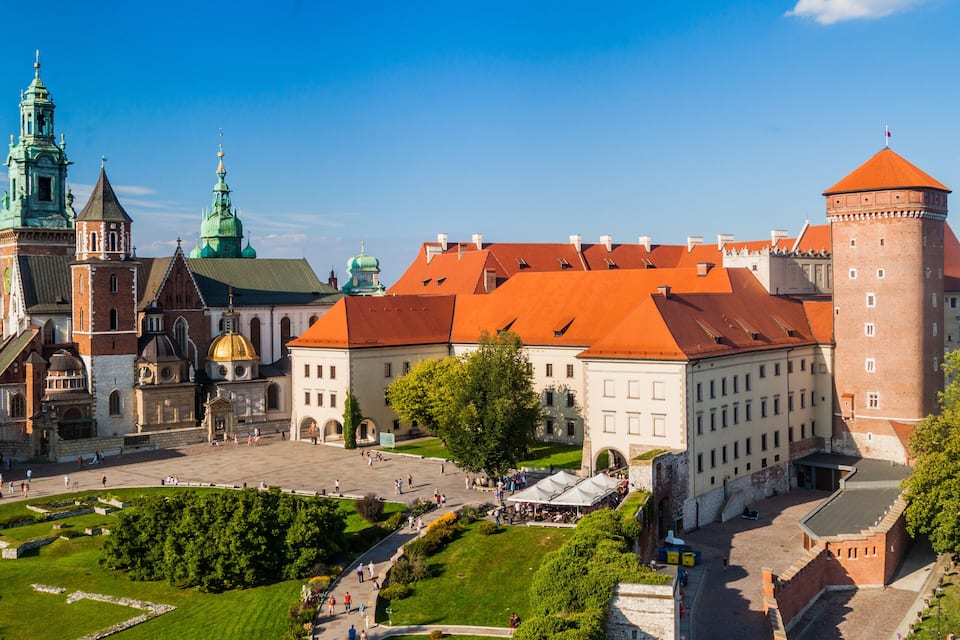 A historic castle with red-tiled roofs, green domes, and a prominent tower.