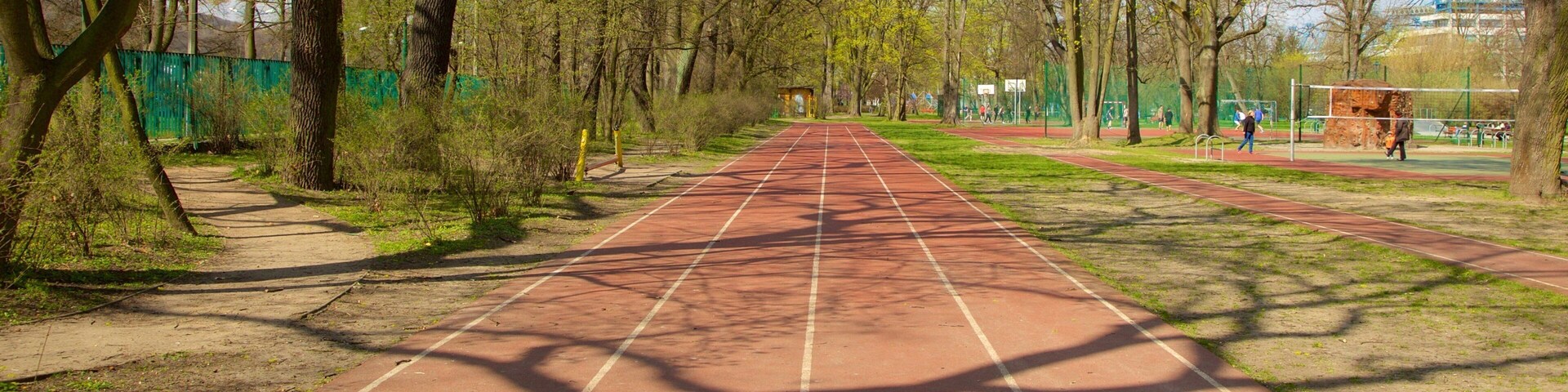 Pista de atletismo com árvores e quadra de basquete ao fundo.