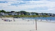 Een strandvolleybalwedstrijd op een zandstrand, met huizen op de achtergrond.