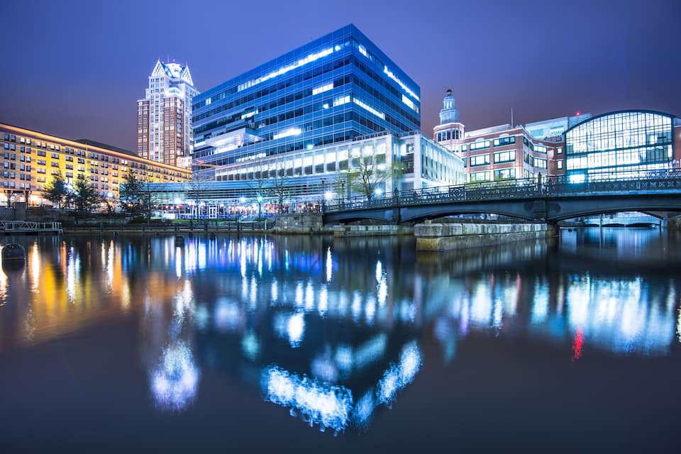 Un paisatge urbà modern amb un riu que reflecteix edificis, un pont i una torre del rellotge.