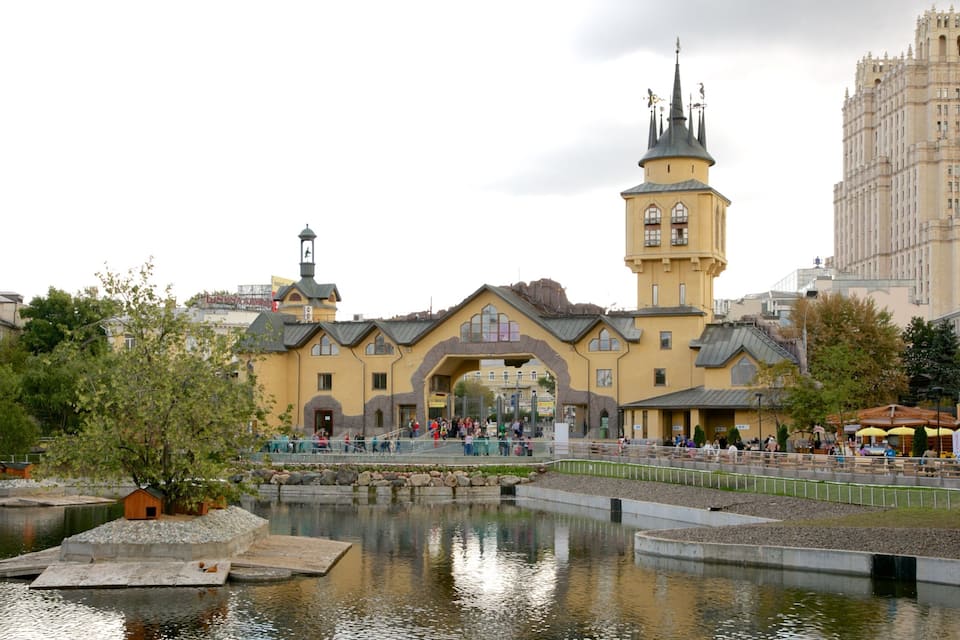 Ein gelbes Gebäude mit einem Turm und einer Uhr, umgeben von einem Teich und Bäumen.