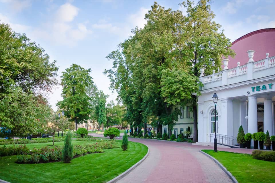 A landscaped garden with a curved pathway, trees, and a building with columns and a dome.