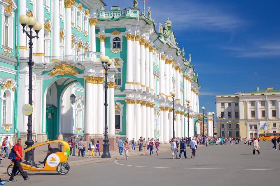 A bustling square with ornate buildings, a yellow tuk-tuk, and pedestrians.