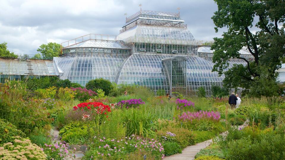 A large glass greenhouse surrounded by a diverse garden with various flowers and plants.