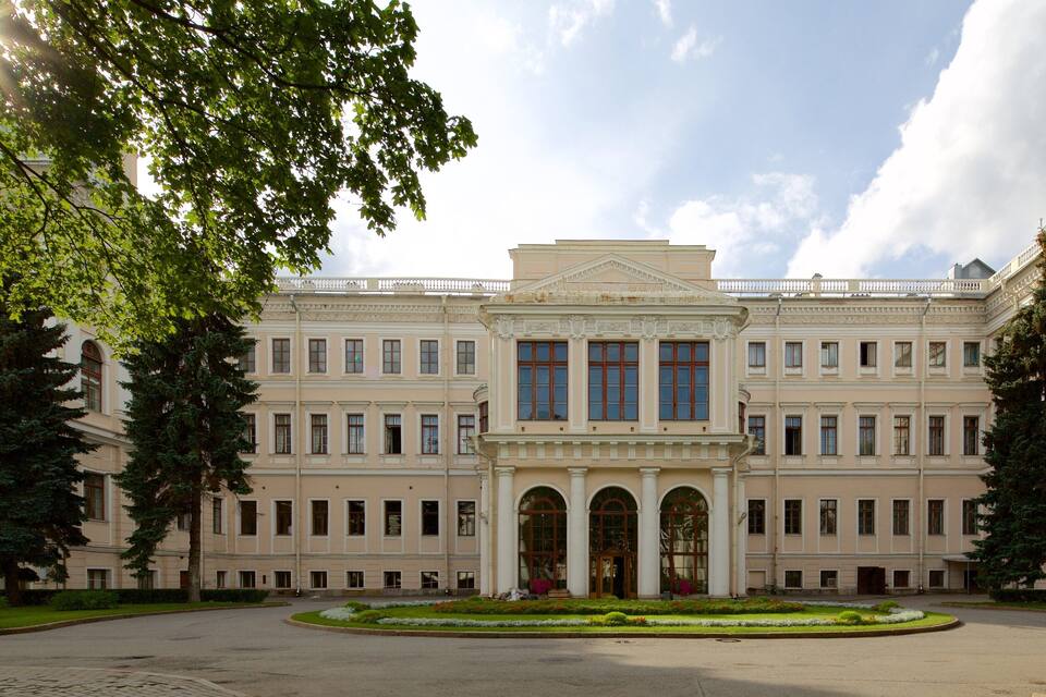 Ein großes, klassizistisches Gebäude mit symmetrischer Architektur, umgeben von gepflegten Gärten und hohen Bäumen.