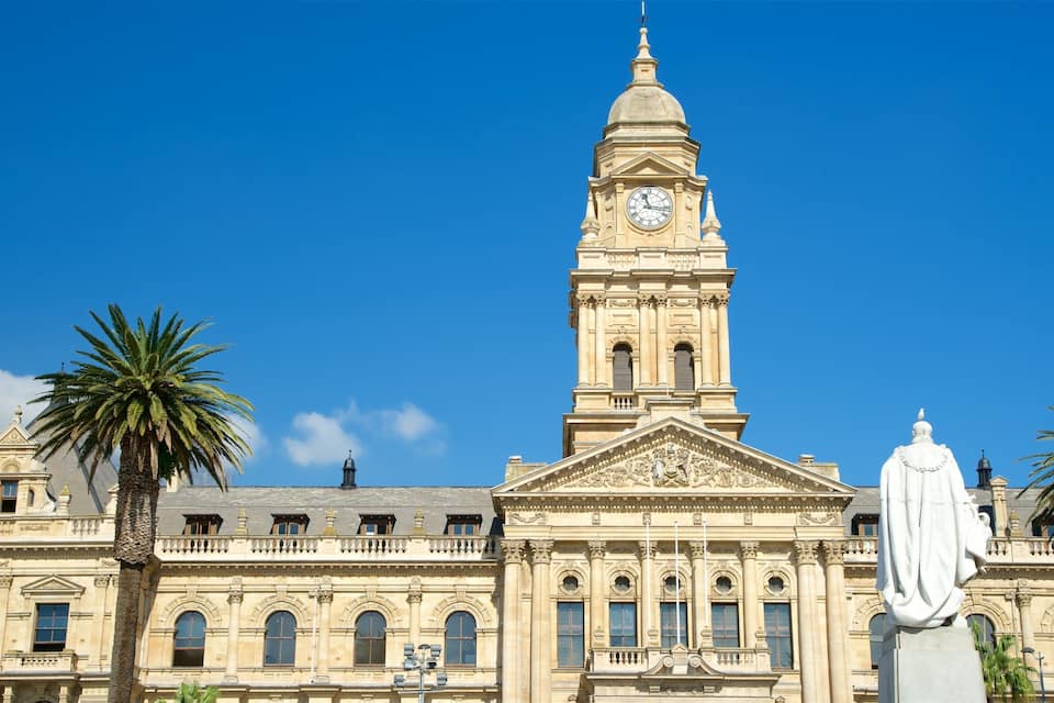 Un edifici històric amb una torre del rellotge, palmeres i una estàtua.