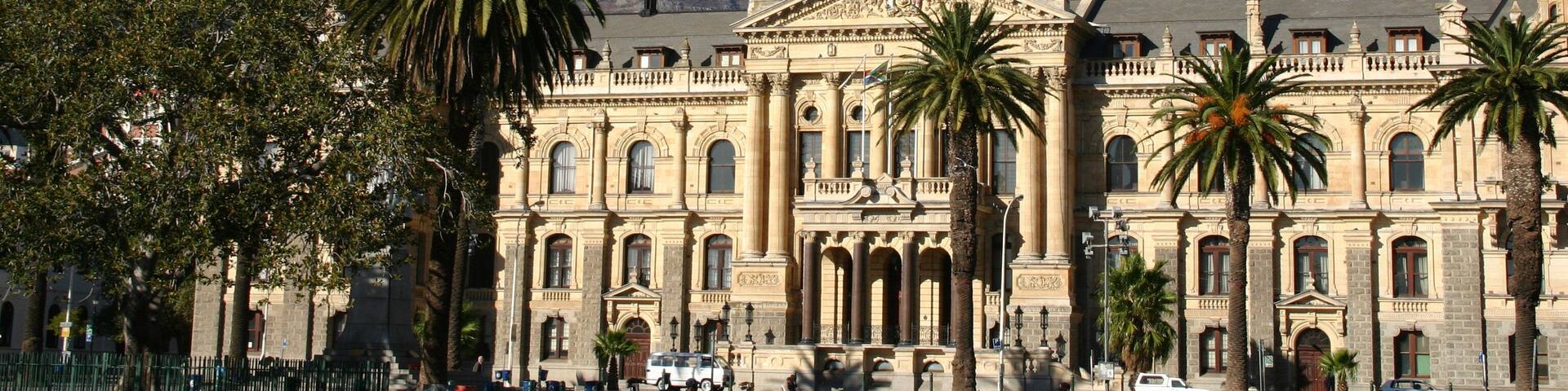 A historic building with a clock tower, palm trees, and a mountain in the background.