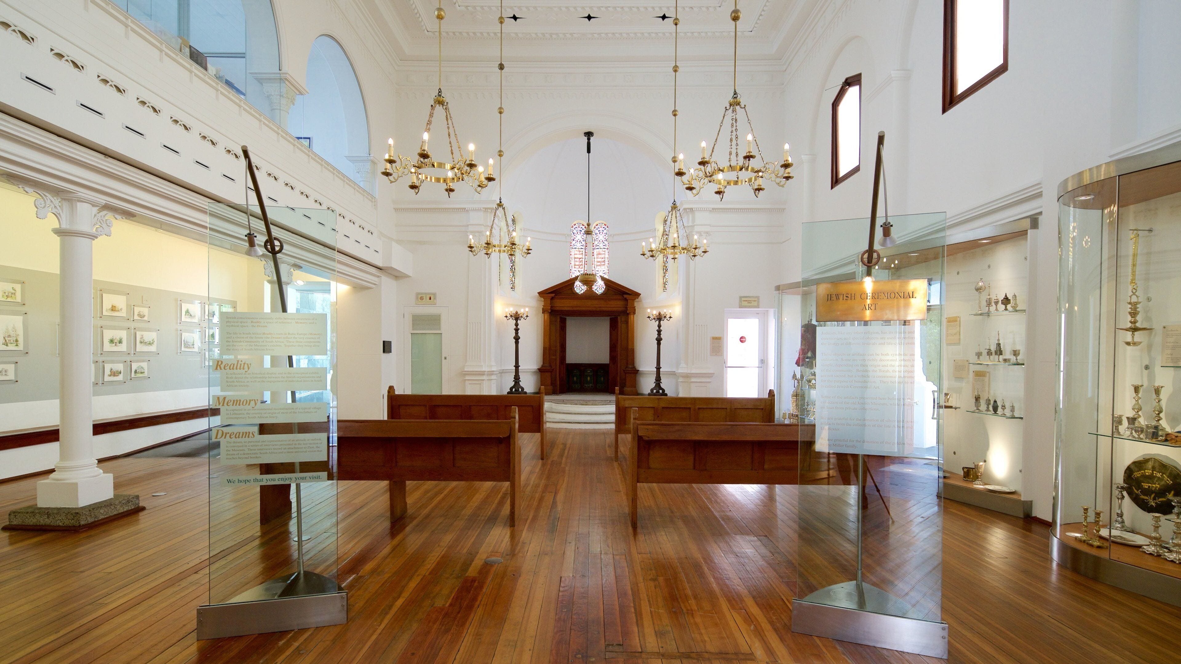 An interior with wooden benches, chandeliers, and glass display cases with artifacts.