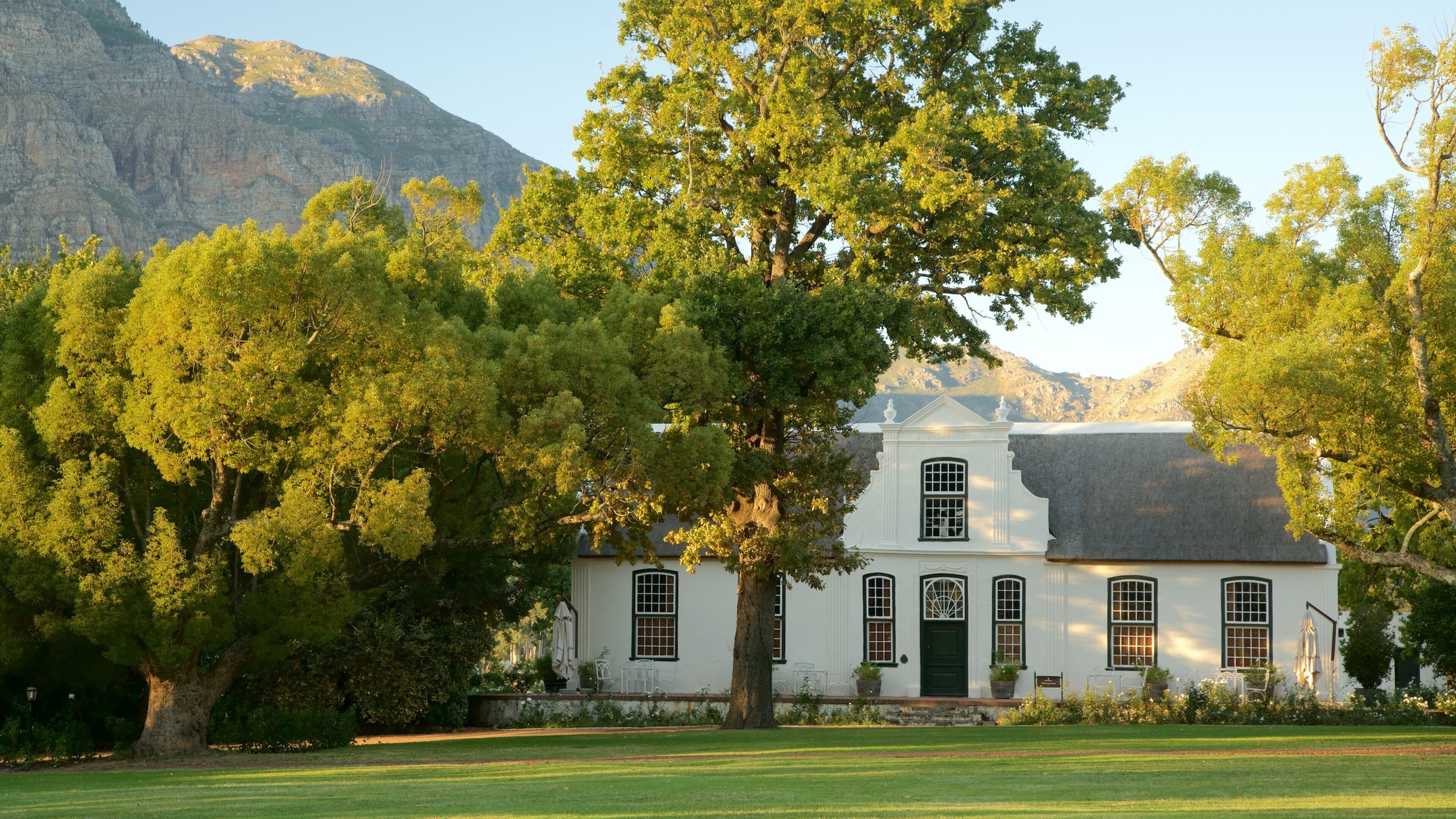 A white colonial-style house with a green door, surrounded by lush trees and a mountain in the background.