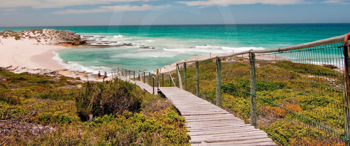 A wooden boardwalk leading to a beach with turquoise waters and rocky outcrops.