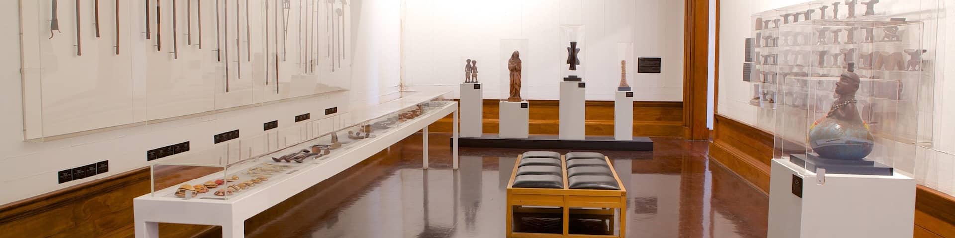 An art gallery with wooden floors and white walls, displaying various sculptures and artifacts.
