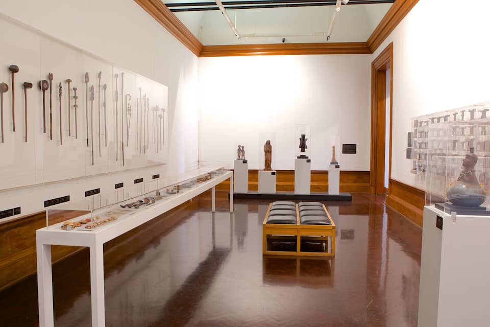 Uma galeria de arte com pisos de madeira e paredes brancas, exibindo diversas esculturas e artefatos.