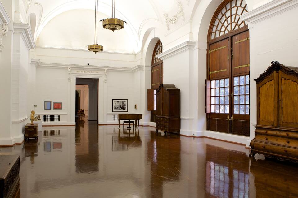 A spacious gallery with high ceilings, wooden floors, and large windows.