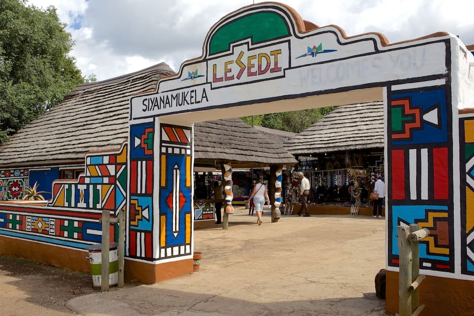 Een kleurrijk toegangshek met 'LESEEDI' en 'SIYANAMUKELA' erop, dat leidt naar een marktgebied.
