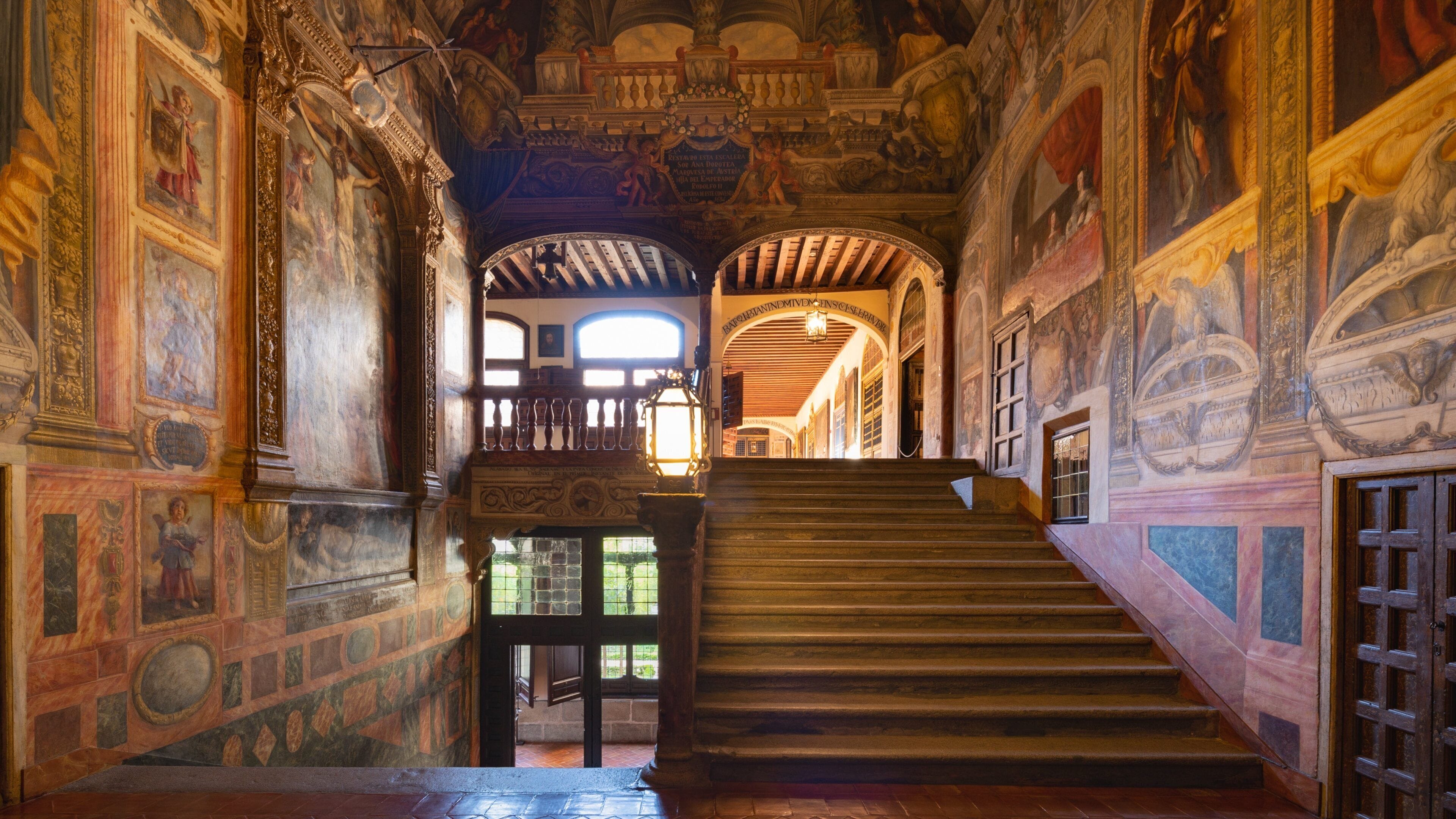 Una majestuosa escalera con frescos ornamentados y detalles arquitectónicos en un edificio histórico.