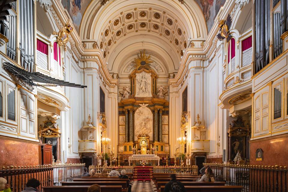 An ornate church interior with a high ceiling, detailed frescoes, and a central altar.