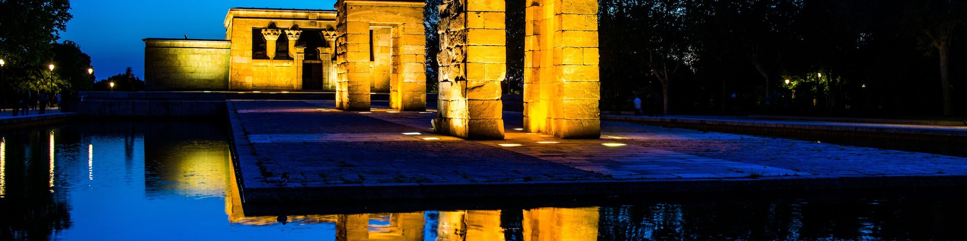 Antiguas estructuras de piedra iluminadas al anochecer, reflejándose en aguas tranquilas.