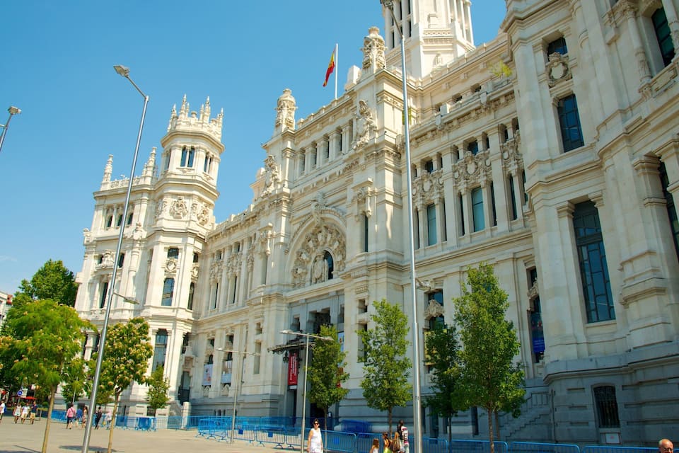 A grand neoclassical building with ornate columns and statues, surrounded by trees and blue barriers.