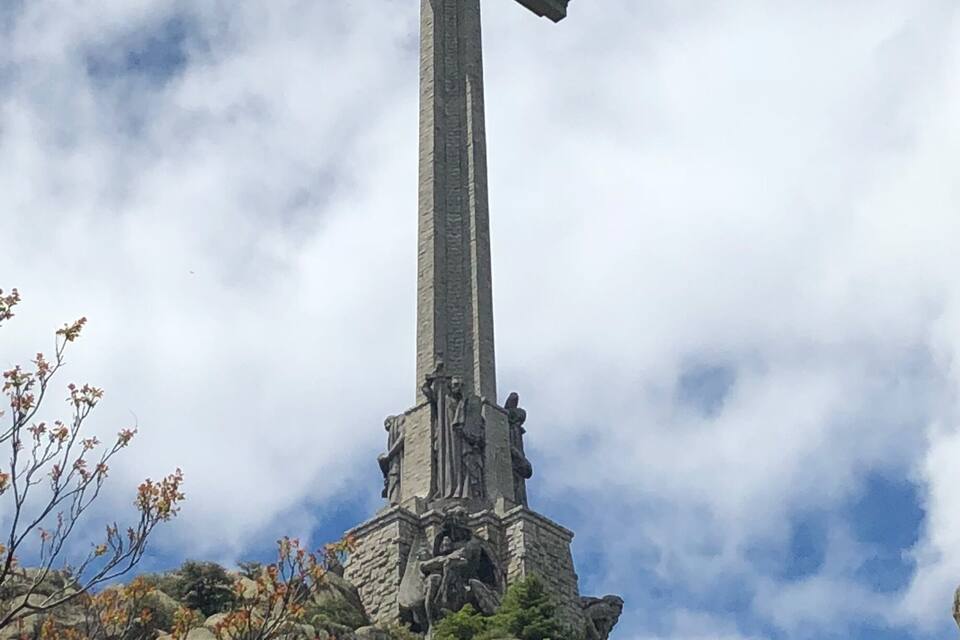 Una gran cruz de piedra sobre una colina rocosa bajo un cielo nublado.