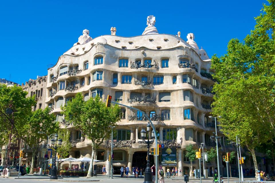 Un edifici singular amb un disseny arquitectònic únic, amb balcons i escultures, envoltat d'arbres i elements urbans.