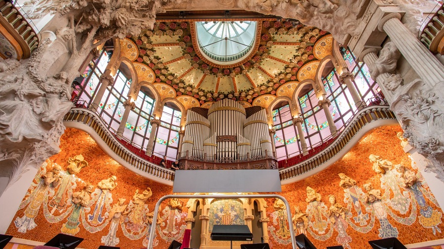 A grand hall with ornate mosaics, a large organ, and a high ceiling with intricate designs.