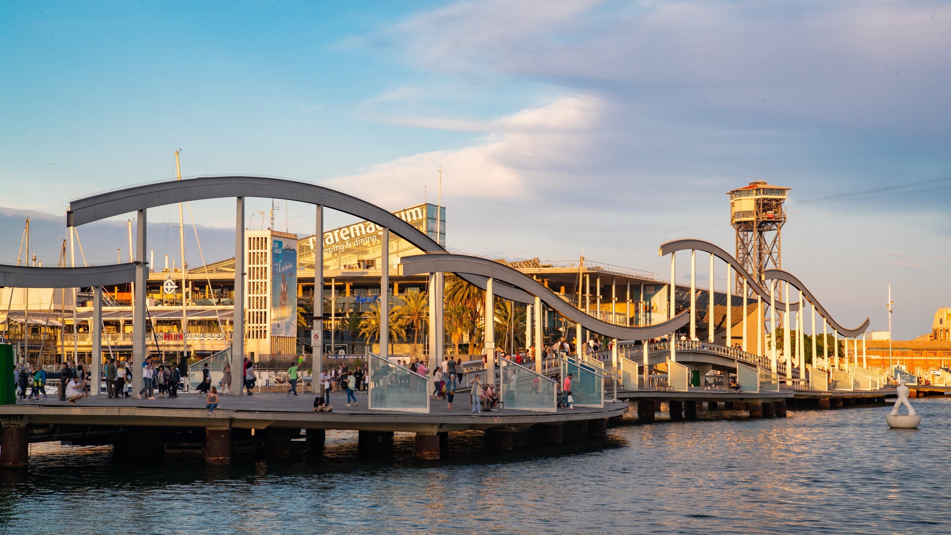 Un paseo marítimo con un puente moderno, un restaurante y una torre.
