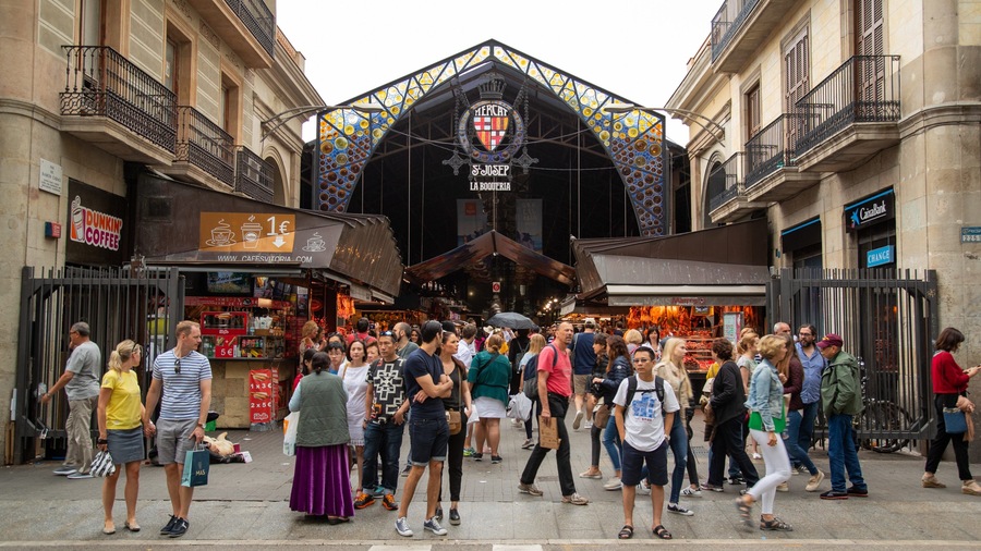 A crowded street with a market stall and a building with a colorful facade.
