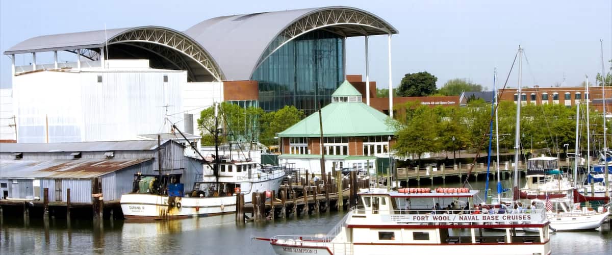 A marina with boats docked, a large modern building with a green roof, and a historic ship named 'DARANA R' in the background.