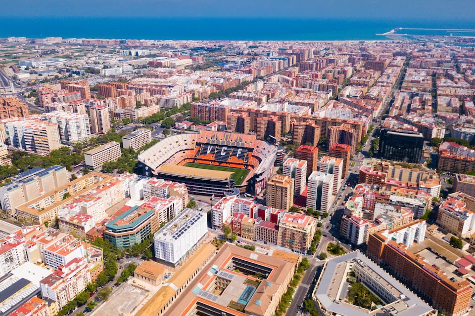 Vue aérienne d’une ville avec un grand stade entouré de bâtiments urbains denses et une côte en arrière-plan.