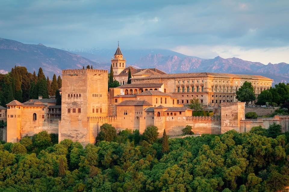 A historic fortress with a prominent tower, surrounded by lush greenery and mountains in the background.