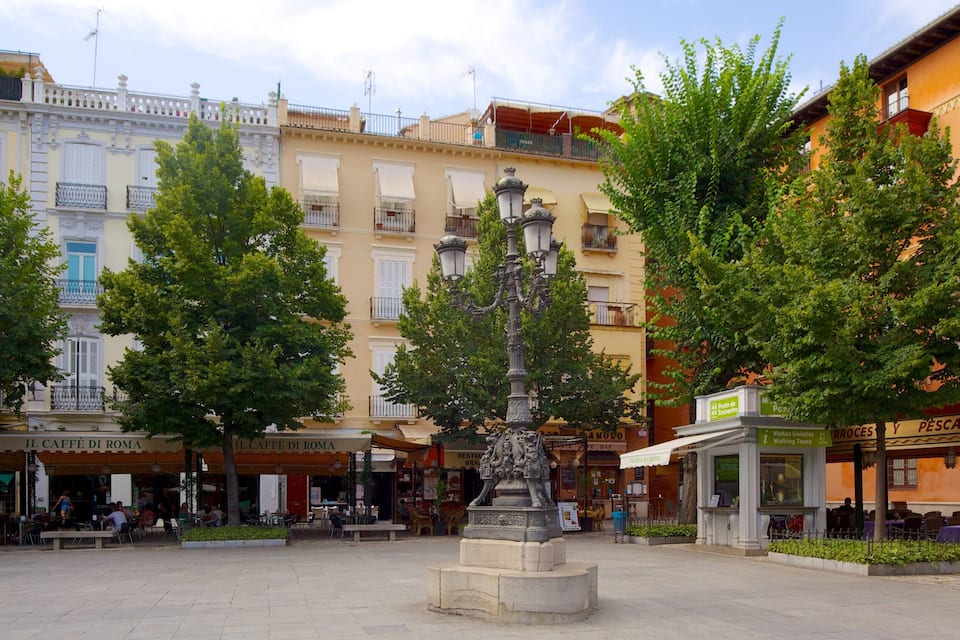 A plaza with a central fountain, surrounded by trees and buildings with cafes and shops.