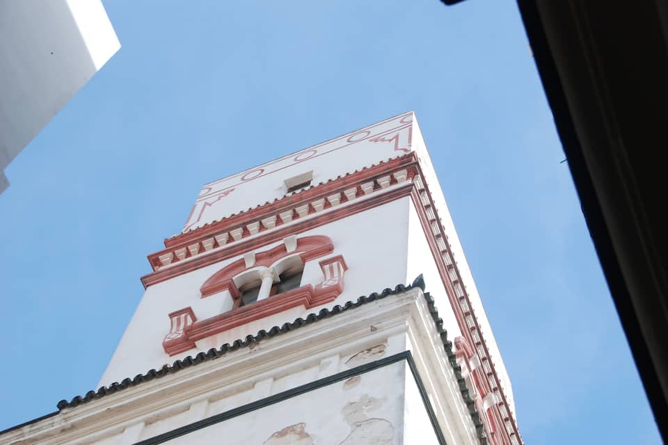 A tower with a white facade and red accents, including a balcony and decorative elements.