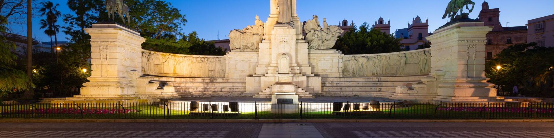 Un monumento grande con una columna central y estatuas a ambos lados, rodeado por una valla y palmeras.
