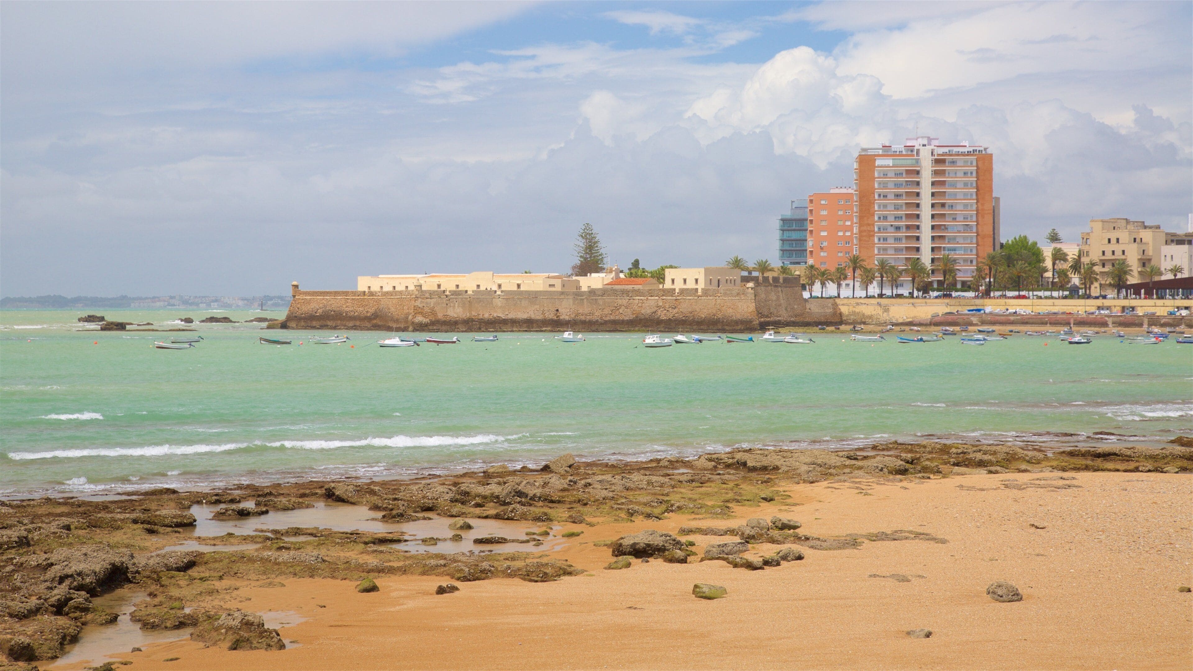 A beach with boats, a fort, and buildings in the background.